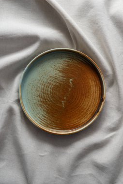 Yuvarlak plaka, bej rengi pamuk masa örtüsünün üzerinde sıcak renklerde bir kenarı var. Yumuşak renk paletinde doğal elementlerle minimalist kompozisyon. El yapımı ahenk konsepti, üst görünüm