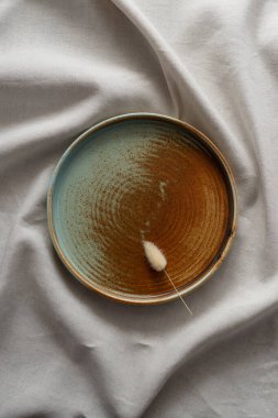 Yuvarlak plaka, bej rengi pamuk masa örtüsünün üzerinde sıcak renklerde bir kenarı var. Yumuşak renk paletinde doğal elementlerle minimalist kompozisyon. El yapımı ahenk konsepti, üst görünüm