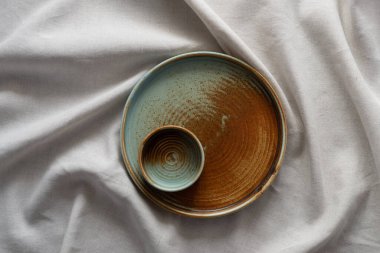 Yuvarlak plaka, bej rengi pamuk masa örtüsünün üzerinde sıcak renklerde bir kenarı var. Yumuşak renk paletinde doğal elementlerle minimalist kompozisyon. El yapımı ahenk konsepti, üst görünüm