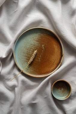 Yuvarlak plaka, bej rengi pamuk masa örtüsünün üzerinde sıcak renklerde bir kenarı var. Yumuşak renk paletinde doğal elementlerle minimalist kompozisyon. El yapımı ahenk konsepti, üst görünüm