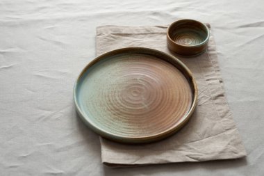 Yuvarlak plaka, bej rengi pamuk masa örtüsünün üzerinde sıcak renklerde bir kenarı var. Yumuşak renk paletinde doğal elementlerle minimalist kompozisyon. El yapımı ahenk konsepti, üst görünüm