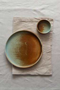 Yuvarlak plaka, bej rengi pamuk masa örtüsünün üzerinde sıcak renklerde bir kenarı var. Yumuşak renk paletinde doğal elementlerle minimalist kompozisyon. El yapımı ahenk konsepti, üst görünüm