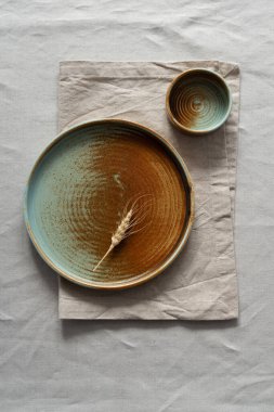 Yuvarlak plaka, bej rengi pamuk masa örtüsünün üzerinde sıcak renklerde bir kenarı var. Yumuşak renk paletinde doğal elementlerle minimalist kompozisyon. El yapımı ahenk konsepti, üst görünüm