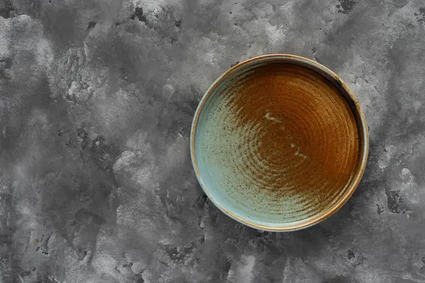 Yuvarlak bir plaka, gri beton arka planda sıcak renklerde bir kenarı var. Yumuşak renk paletinde doğal elementlerle minimalist kompozisyon. El yapımı ahenk konsepti, üst görünüm