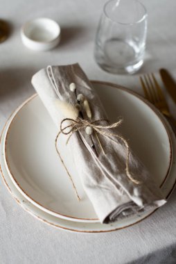 Bahar minimalist masası sıcak ve nötr renklerde. Paskalya bayramı masa dekorasyonu, beyaz tabaklar, altın çatal bıçak takımı, mumlar, yumurtalar ve vazodaki söğüt dalları. Paskalya aile yemeği ya da kahvaltı konsepti