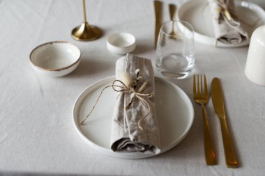 Bahar minimalist masası sıcak ve nötr renklerde. Paskalya bayramı masa dekorasyonu, beyaz tabaklar, altın çatal bıçak takımı, mumlar, yumurtalar ve vazodaki söğüt dalları. Paskalya aile yemeği ya da kahvaltı konsepti