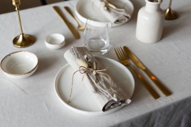 Bahar minimalist masası sıcak ve nötr renklerde. Paskalya bayramı masa dekorasyonu, beyaz tabaklar, altın çatal bıçak takımı, mumlar, yumurtalar ve vazodaki söğüt dalları. Paskalya aile yemeği ya da kahvaltı konsepti