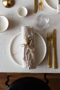 Bahar minimalist masası sıcak ve nötr renklerde. Paskalya bayramı masa dekorasyonu, beyaz tabaklar, altın çatal bıçak takımı, mumlar, yumurtalar ve vazodaki söğüt dalları. Paskalya aile yemeği ya da kahvaltı konsepti