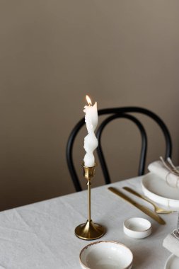 Bahar minimalist masası sıcak ve nötr renklerde. Paskalya bayramı masa dekorasyonu, beyaz tabaklar, altın çatal bıçak takımı, mumlar, yumurtalar ve vazodaki söğüt dalları. Paskalya aile yemeği ya da kahvaltı konsepti