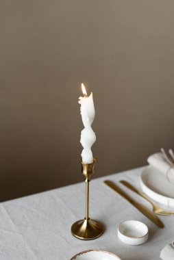 Bahar minimalist masası sıcak ve nötr renklerde. Paskalya bayramı masa dekorasyonu, beyaz tabaklar, altın çatal bıçak takımı, mumlar, yumurtalar ve vazodaki söğüt dalları. Paskalya aile yemeği ya da kahvaltı konsepti