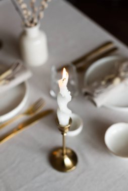 Bahar minimalist masası sıcak ve nötr renklerde. Paskalya bayramı masa dekorasyonu, beyaz tabaklar, altın çatal bıçak takımı, mumlar, yumurtalar ve vazodaki söğüt dalları. Paskalya aile yemeği ya da kahvaltı konsepti