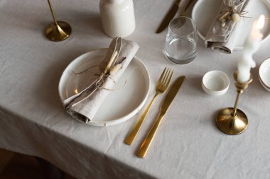 Bahar minimalist masası sıcak ve nötr renklerde. Paskalya bayramı masa dekorasyonu, beyaz tabaklar, altın çatal bıçak takımı, mumlar, yumurtalar ve vazodaki söğüt dalları. Paskalya aile yemeği ya da kahvaltı konsepti
