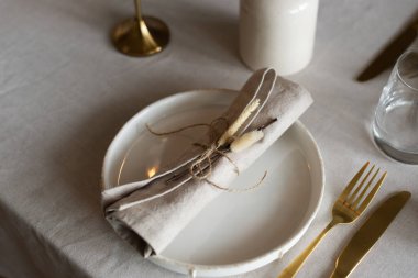 Bahar minimalist masası sıcak ve nötr renklerde. Paskalya bayramı masa dekorasyonu, beyaz tabaklar, altın çatal bıçak takımı, mumlar, yumurtalar ve vazodaki söğüt dalları. Paskalya aile yemeği ya da kahvaltı konsepti