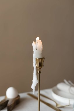 Bahar minimalist masası sıcak ve nötr renklerde. Paskalya bayramı masa dekorasyonu, beyaz tabaklar, altın çatal bıçak takımı, mumlar, yumurtalar ve vazodaki söğüt dalları. Paskalya aile yemeği ya da kahvaltı konsepti