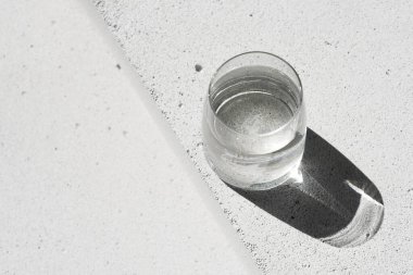 Tarafsız beton zemin üzerinde saf su ve estetik güneş ışığı gölgesi olan cam. Saflık ve sadelik sahnesi. Üst görünüm, alanı kopyala