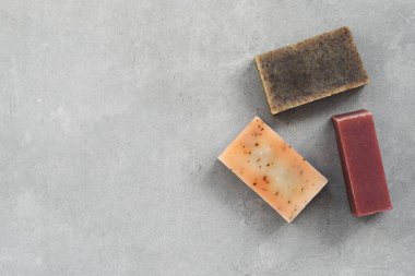Minimalist beton arka planda dizilmiş üç doğal el yapımı sabun tonu. Cilt bakımı, kaplıca, sağlık ve çevre dostu yaşam temaları için temiz kompozisyon