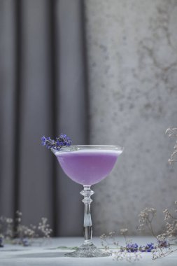 Elegant glass of Lavender Cocktail or mocktails surrounded by ingredients and fresh lavender and gypsophila flowers on gray table surface. Refreshing drink ready for drinking. clipart