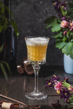 Koyu ahşap masa yüzeyindeki malzemeler ve bar aletleriyle çevrili New York ekşi kokteylini tazeleyen bir bardak.