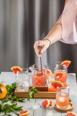 Grapefruit kokteyli hazırlayan gerçek bir kadın. İçindekiler ve açık gri masa yüzeyindeki bar aletleriyle çevrili kokteyller. İçmeye hazırım.