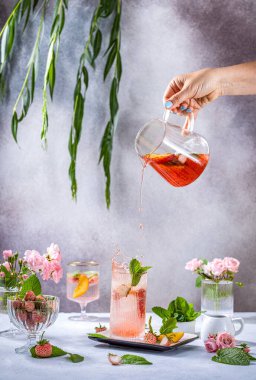 Şeftali, akçaağaç şurubu, taze nane ve böğürtlenli limonata, viski bardağında veya açık gri masa yüzeyindeki malzemeler ve bar aletleriyle çevrili mocktail kokteyli.