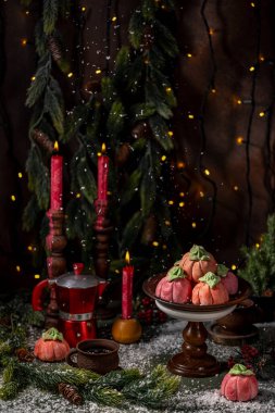 Noel süslemeleri ile çevrili balkabağı şeklinde ev yapımı pembe şekerlemeler. Koyu renk arka plan, mumlar, elektrik çelenkleri. Yeni yıl tebrik kartı..