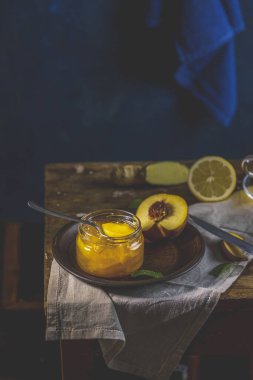 Taze ev yapımı şeftali reçeli kavanoza doluyor. Eski karanlık kırsal sihir tarzı. Güneşli bir ışık. Yanında birkaç taze meyve, limon ve nane var..