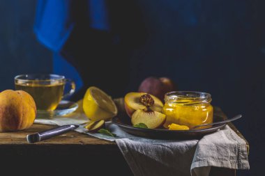 Taze ev yapımı şeftali reçeli kavanoza doluyor. Eski karanlık kırsal sihir tarzı. Güneşli bir ışık. Yanında birkaç taze meyve, limon ve nane var..