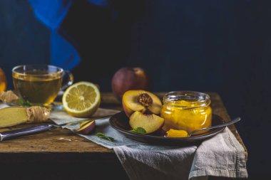 Taze ev yapımı şeftali reçeli kavanoza doluyor. Eski karanlık kırsal sihir tarzı. Güneşli bir ışık. Yanında birkaç taze meyve, limon ve nane var..
