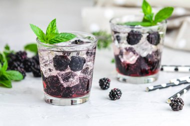 Buzlu ve nane yapraklı böğürtlen kokteyli beyaz masada servis ediliyor.