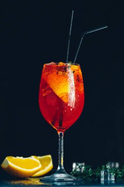 Barda duran aperol spreyini tazeleyen siyah arka planda buz küpleri ve portakal dilimleri.