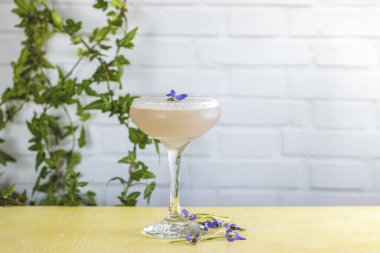 Pembe kokteyl sarı masanın üzerinde duruyor. Mor çiçeklerle süslenmiş.