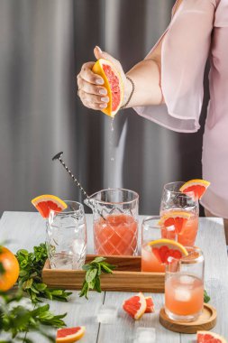 Kadın ferahlatıcı bir yaz kokteyli yapmak için kokteyl bardağına taze greyfurt suyu sıkıyor.