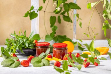 İki kavanoz çilek reçeli taze malzemelerle çevrili, canlı ve iştah açıcı bir sahne oluşturuyor.