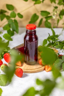 İki şişe çilek suyu taze çilek ve yapraklarla çevrili tahtada duruyor.