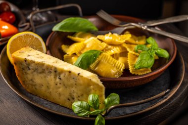 Canlı yeşil fesleğen yapraklarıyla süslenmiş ve yanında cömert bir peynir kamışı eşliğinde yeni pişmiş bir ravioli tabağı sunan köylü ve davetkar bir manzara.