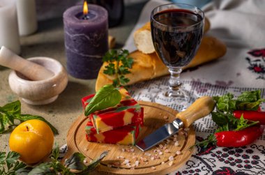 Ahşap bir tahtada fesleğenli kırmızı pesto peyniri ve romantik bir akşam yemeği için bir bardak kırmızı şarap ve baget.