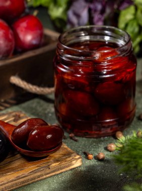 Cam kavanozda turşulu erikler ve tahta kutuda taze kırmızı erikler. Kış için erikleri muhafaza ediyorlar.