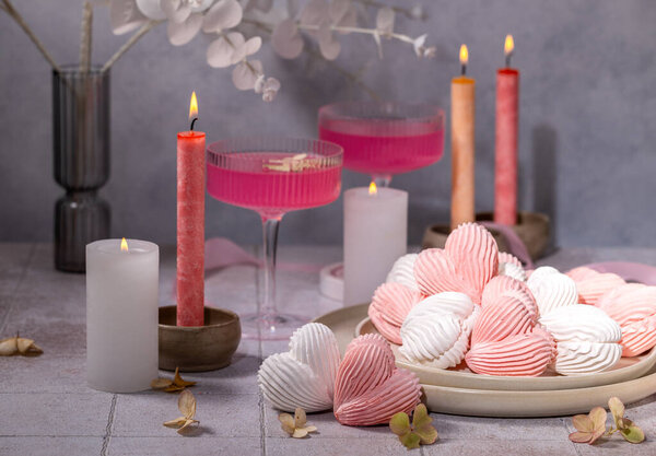 Romantic atmosphere with heart-shaped meringues, pink cocktails, and lit candles, perfect for valentine's day or a special occasion