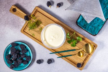 Kremalı beyaz yoğurtlu plastik kap mı yoksa böğürtlenli tatlı mı, ahşap kesme tahtasındaki dereotu ve maydanozlu altın kaşıklarla mı?