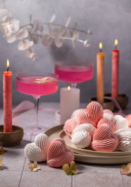 Romantik masa ortamında pembe kokteyller, mumlar ve kalp şeklinde kremalar, tatlı ve güzel bir atmosfer yaratıyor.