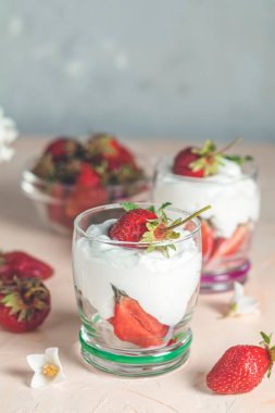 İki bardak katmanlı çilek ve krem peynirle süslenmiş taze çilek ve pembe arka planda yasemin çiçekleri.