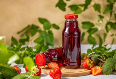 İki şişe taze çilek suyu taze çilek ve nane yapraklarıyla çevrili ahşap bir tahtanın üzerinde oturup canlı ve sağlıklı bir sahne yaratıyor.