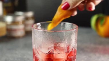 Profesyonel bayan barmen titizlikle taze portakal kabuğunu tipik negroni kokteyline dökerek, karışımbilim uzmanlığını ve içki hazırlığını vurguluyor.