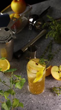 Elma kokteyli kekik filizi ve elma dilimleriyle süslenir, bar tezgahında taze malzemelerin ve bar aletlerinin arasında durur.