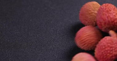 Olgun kırmızı lychees yumuşak dokulu karanlık yüzey boyunca yuvarlanan taze tropikal meyve canlı renk ve pürüzsüz cilt detay sergiler