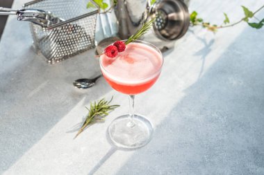 Taze ahududu ve biberiye filizleriyle süslenmiş, parlak bir bar tezgahında zarif cam eşyalar içinde servis edilen yonca kulübü kokteyli.