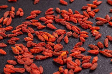 Koyu bir yüzeye yayılmış sayısız kuru kurt üzümü canlı kırmızı renklerini ve desenli görünüşlerini sergiliyor.