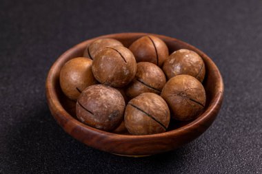 Kabuklu Macadamia fındıkları küçük ahşap kasede oturup karanlık arka planda iştah açıcı bir düzenleme yapıyor.