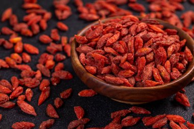 Tahta kase, sağlıklı beslenme ve doğal malzemelerin özünü yakalamak için karanlık bir yüzeye saçılmış canlı, kurumuş goji üzümleriyle dolup taşıyor.