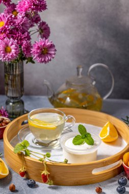 Bitki çayı, kremalı yoğurt, taze meyve ve ahşap tepside canlı çiçeklerle huzurlu bir anın tadını çıkarıyorum.